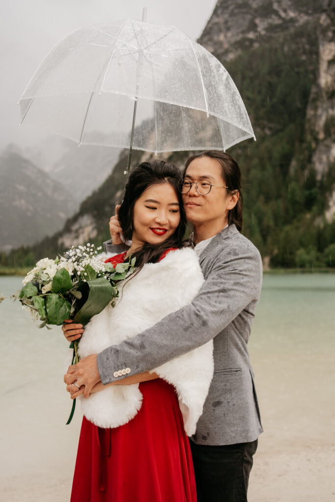 Couple embracing under umbrella with bouquet.