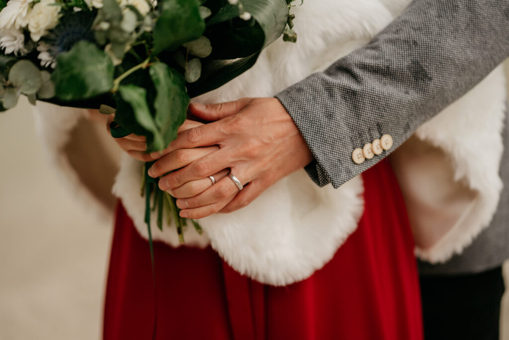 Hands holding bouquet, wearing wedding rings.