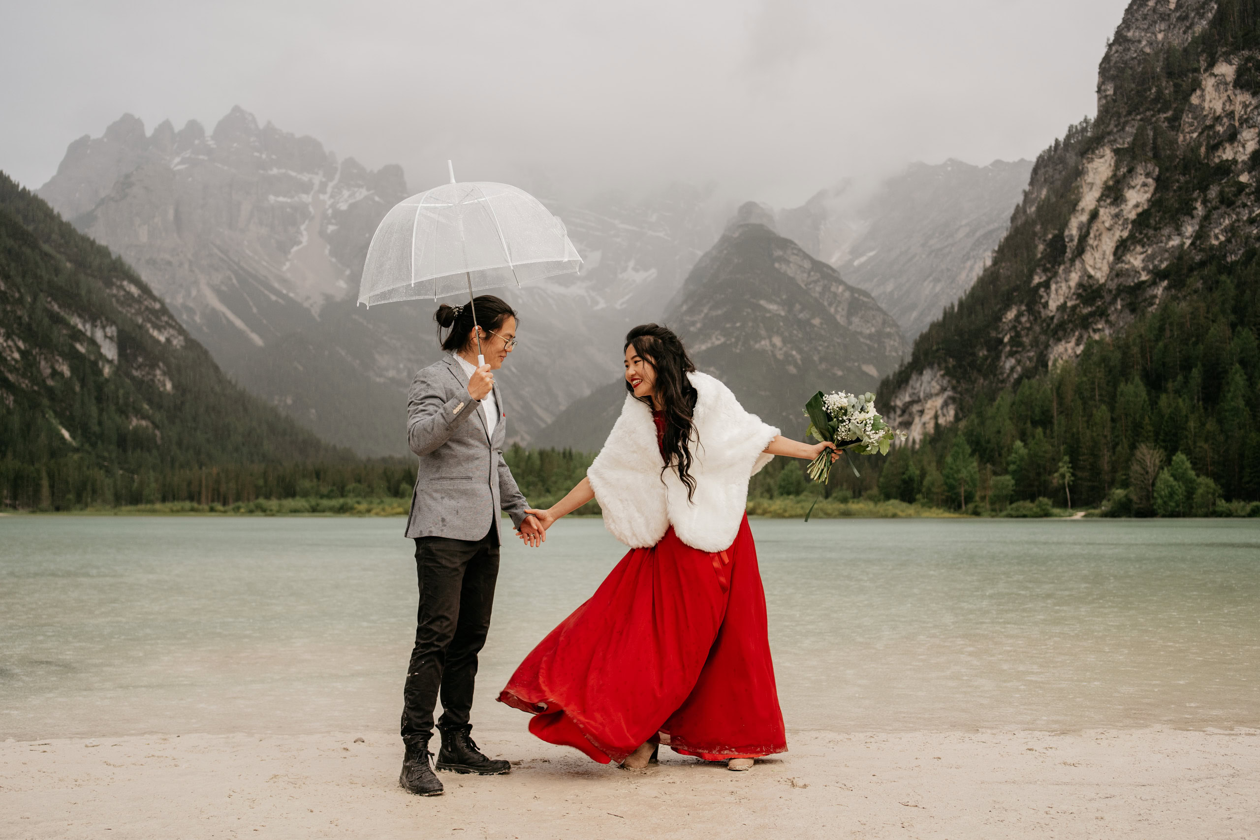 Couple celebrating by a mountain lake under umbrella.