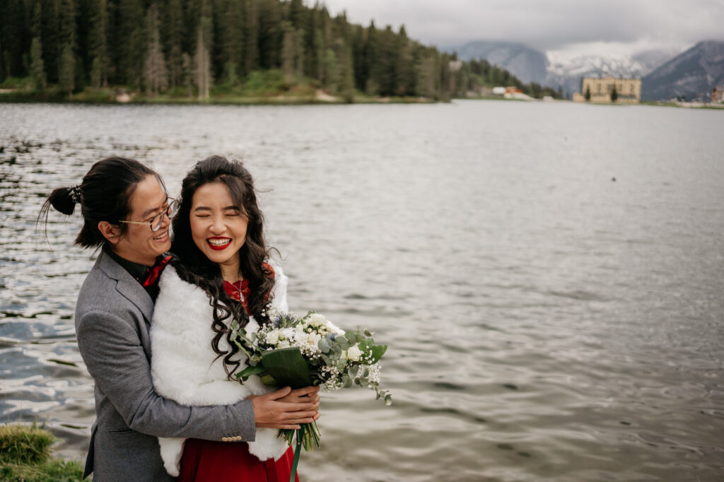 Couple smiling by a lake with mountains behind.