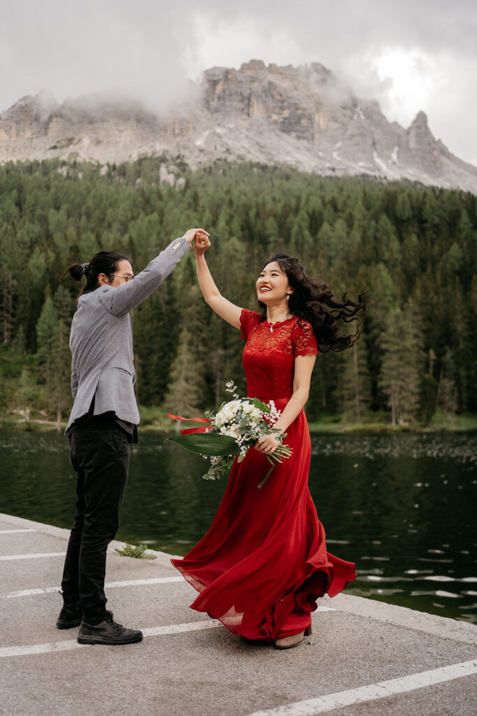 Couple dancing by a mountain lake, holding hands.