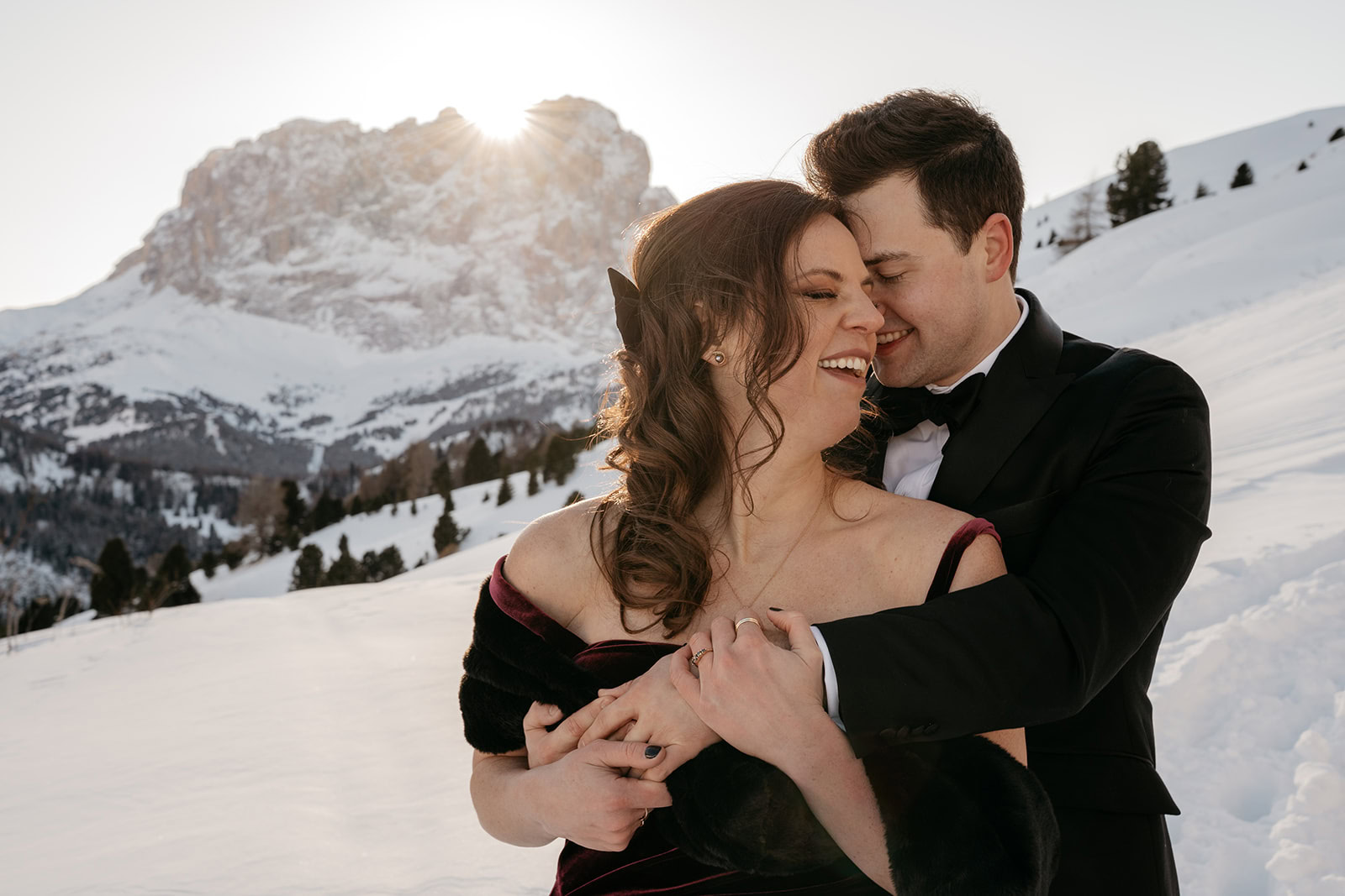Couple embracing in snowy mountain landscape at sunset.