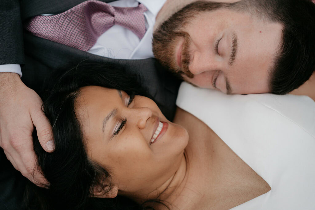 Smiling couple cuddling, eyes closed, in wedding attire.