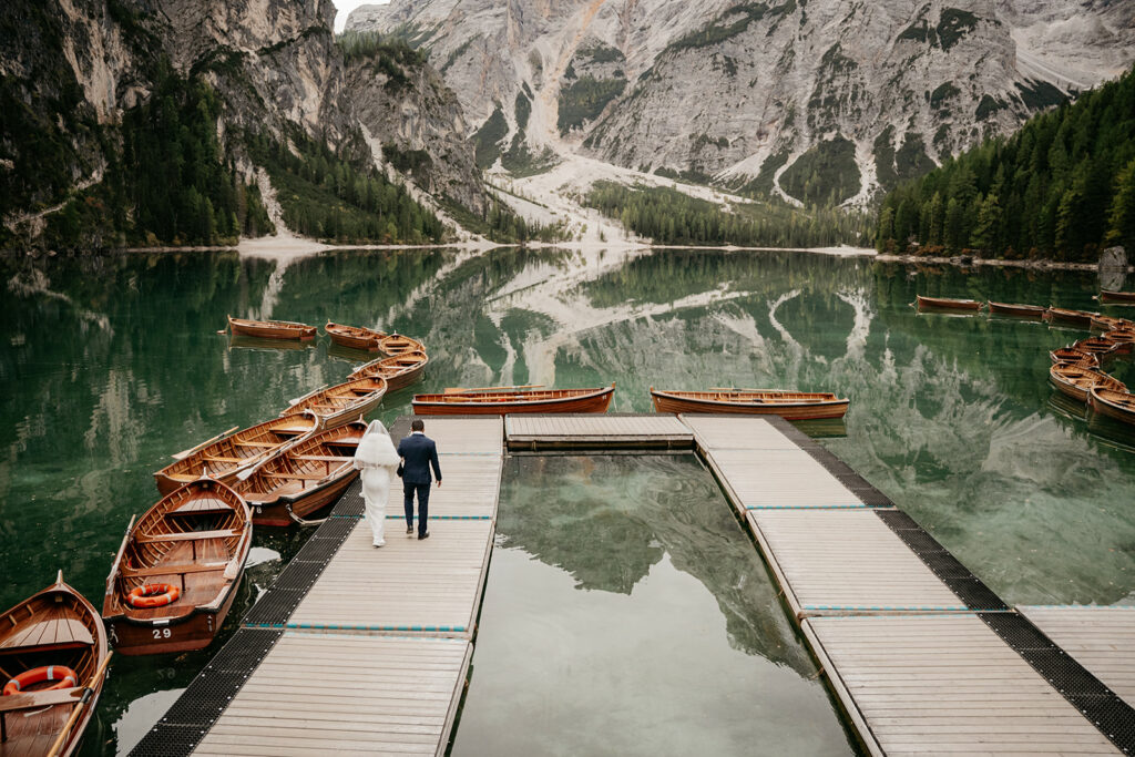 Couple on dock with boats, mountain reflection, serene lake