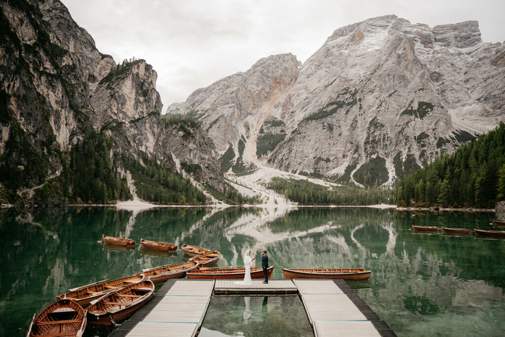 Bride and groom on dock, mountain lake backdrop.