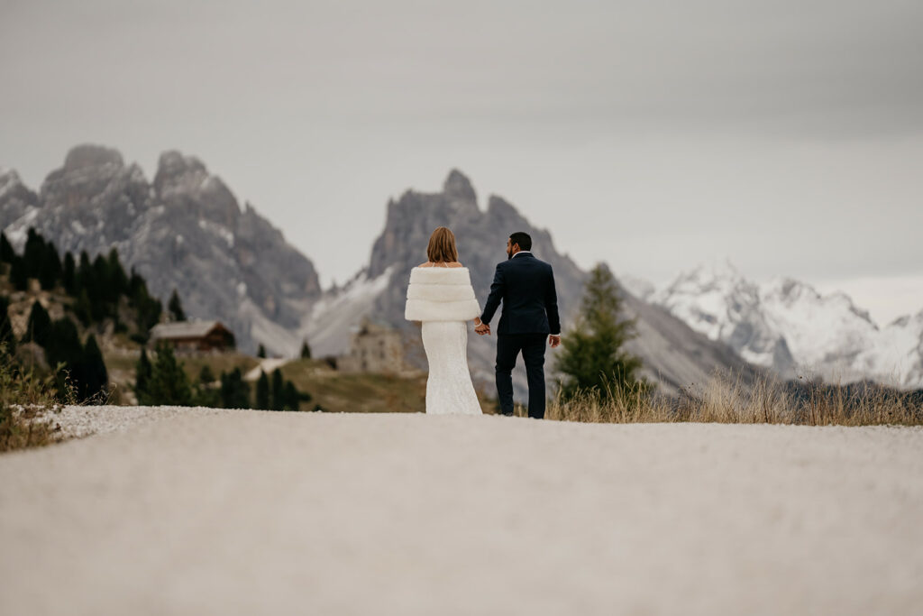 Couple in wedding attire, mountain landscape backdrop.
