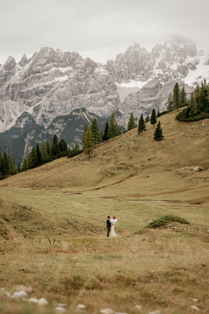 Couple embraces on mountain landscape under cloudy sky.