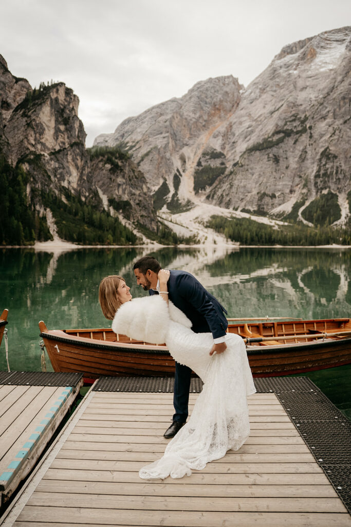 Couple poses romantically by lake and mountains.