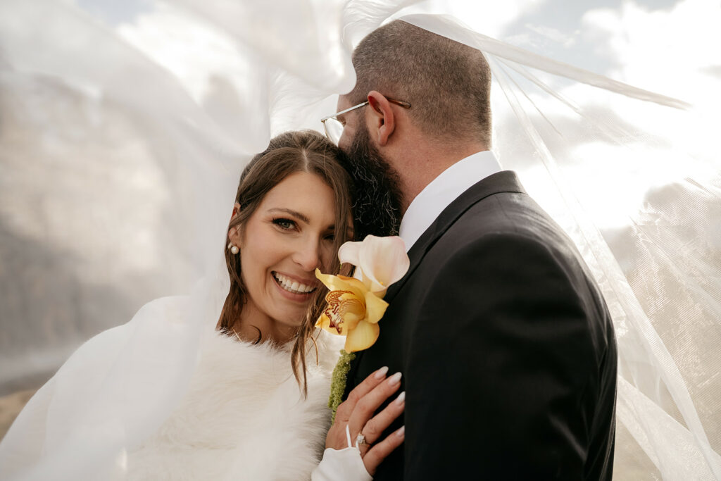 Smiling bride and groom under wedding veil.