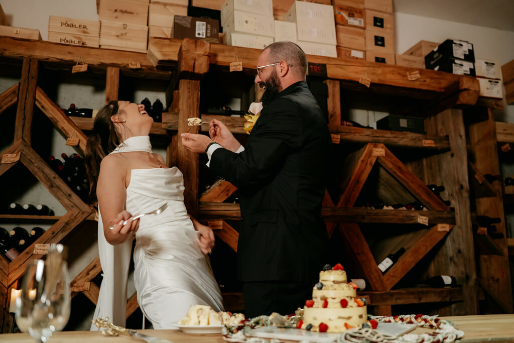 Couple feeding each other cake in wine cellar.
