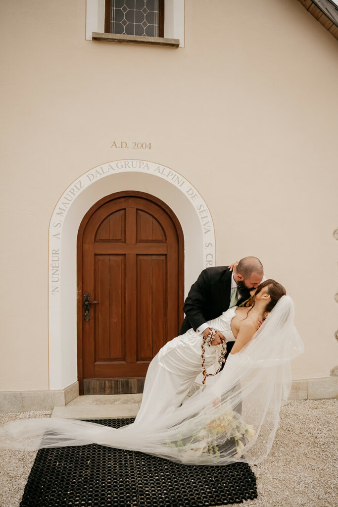 Bride and groom kissing outside a chapel.