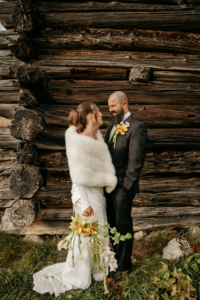 Bride and groom smiling in front of log cabin.