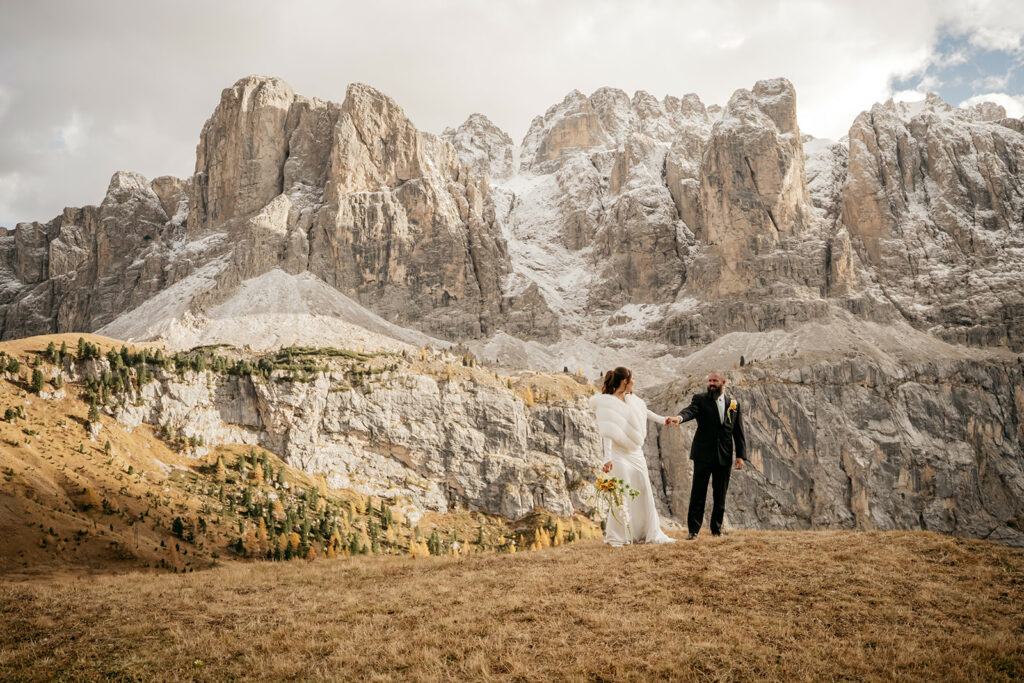 Bride and groom holding hands by mountain cliff.