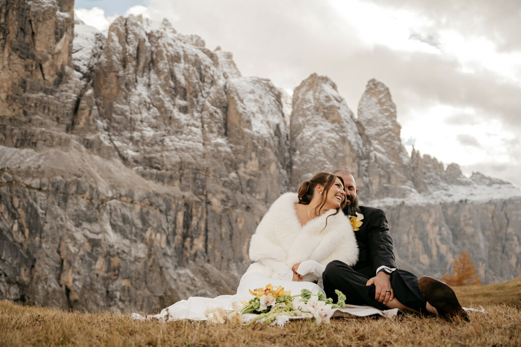 Couple sitting by snowy mountains, smiling.
