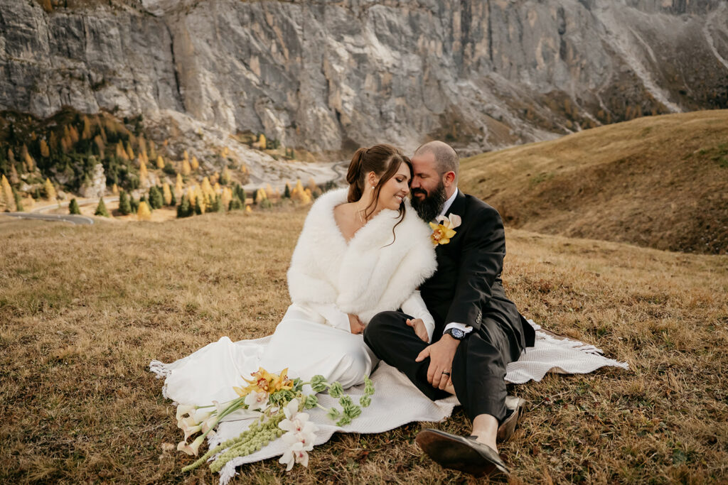 Couple cuddling outdoors with mountain backdrop.