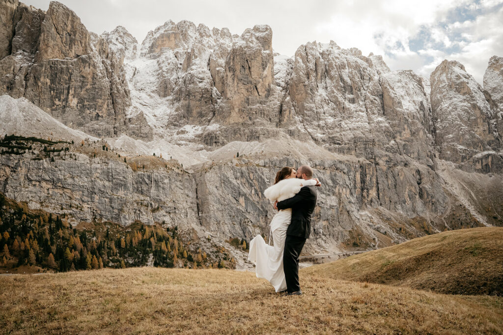 Bride and groom embracing before stunning mountain backdrop.