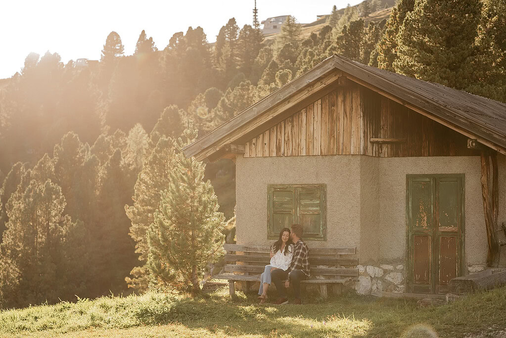 Couple sitting on bench outside rustic cabin in forest.