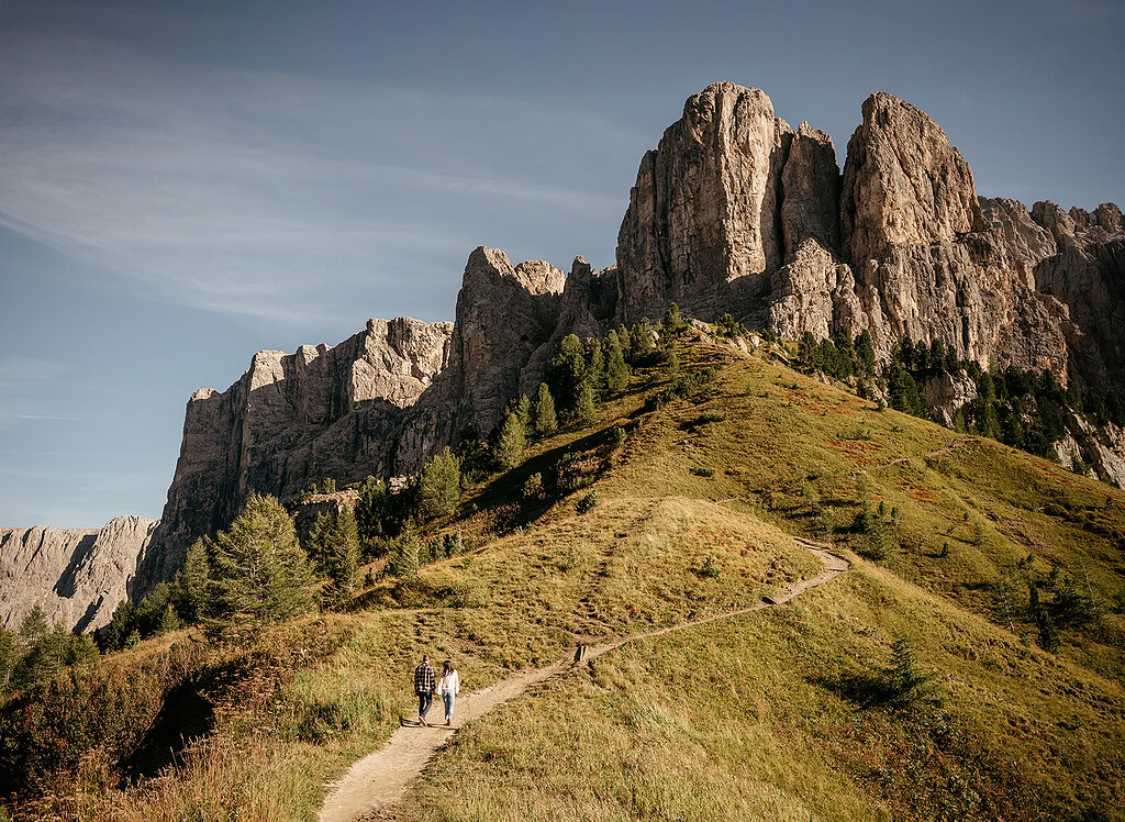Hikers on mountain trail beneath rocky cliffs.
