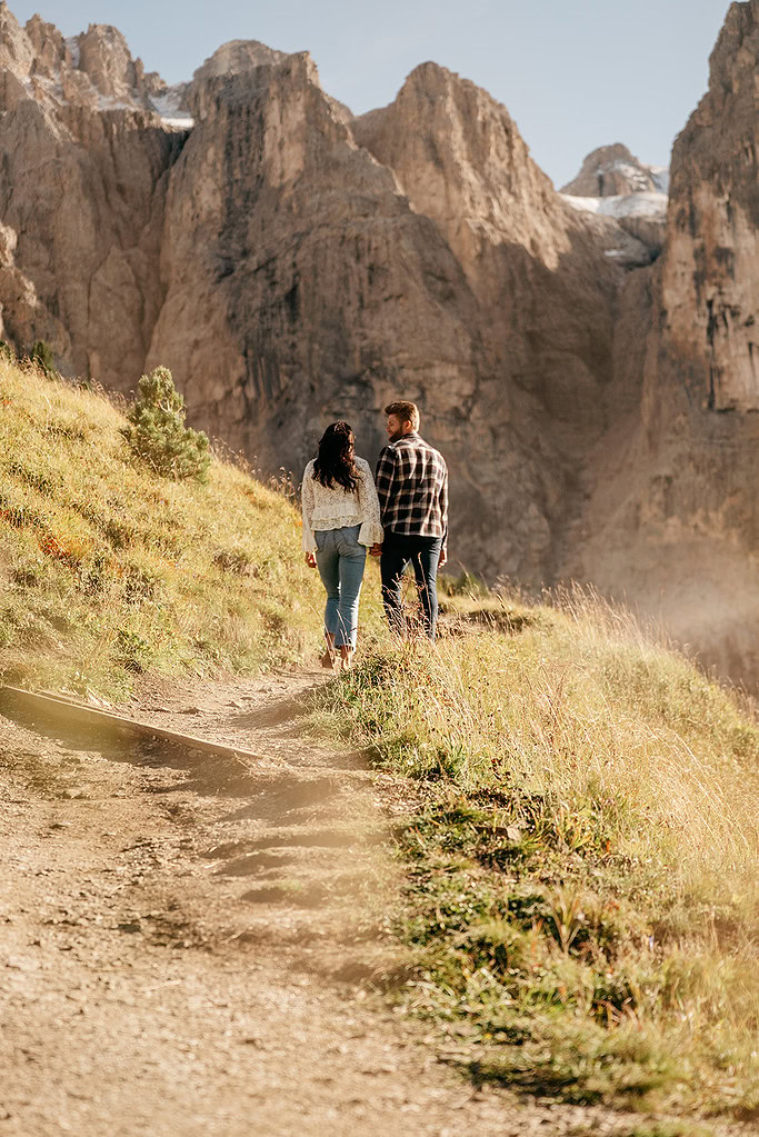 Couple hiking on mountain trail, sunny day.