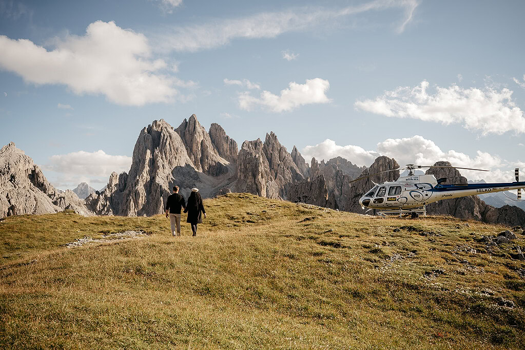 Couple walking near mountains with helicopter nearby.