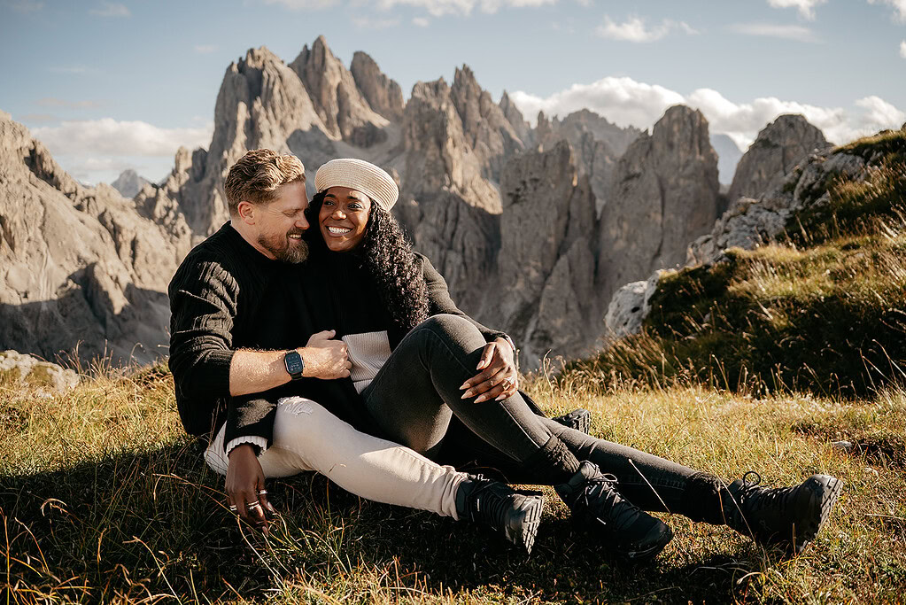 Couple sitting on grass with mountain background.