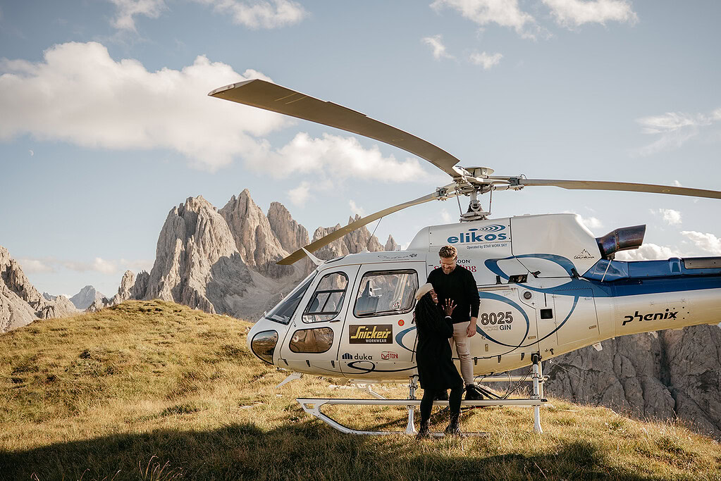 Couple by helicopter in scenic mountain landscape.