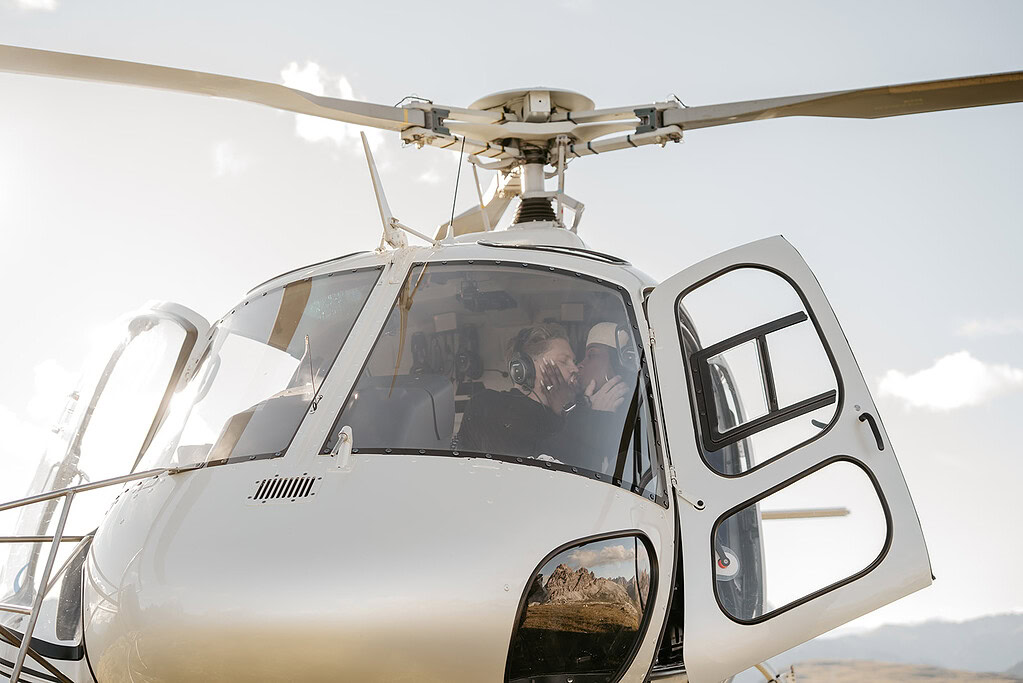 Couple kissing inside helicopter with open door.