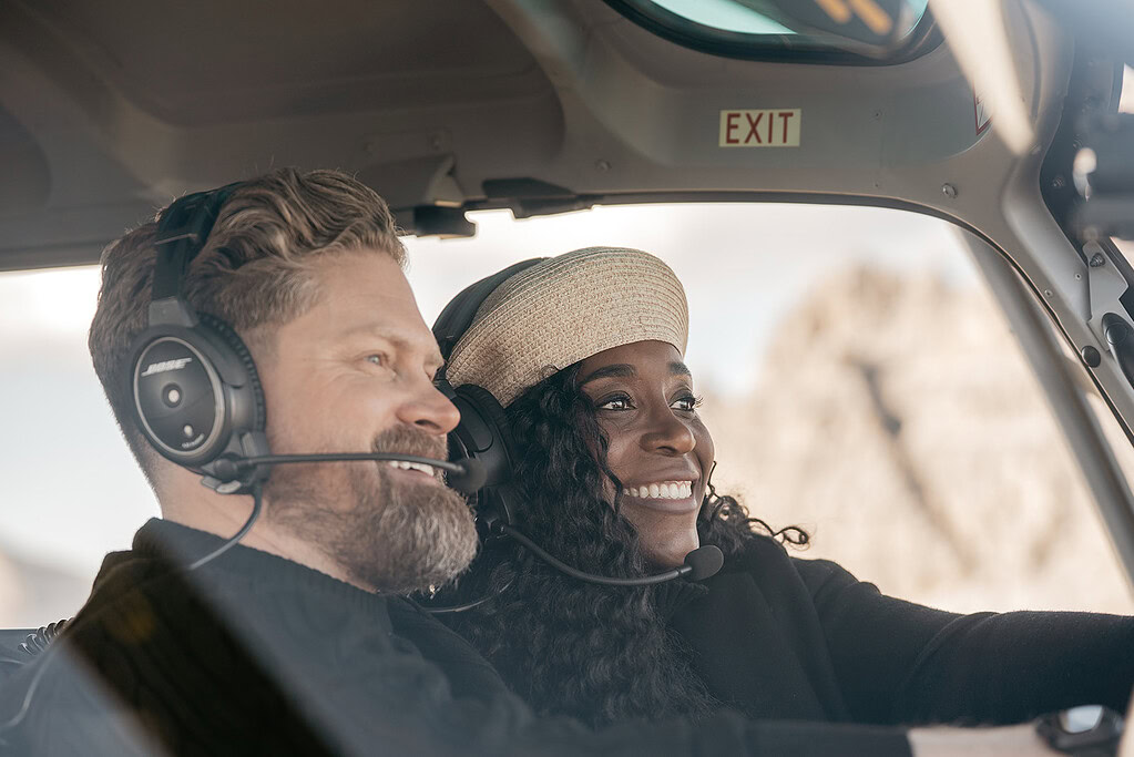 Two people smiling in a helicopter cockpit.