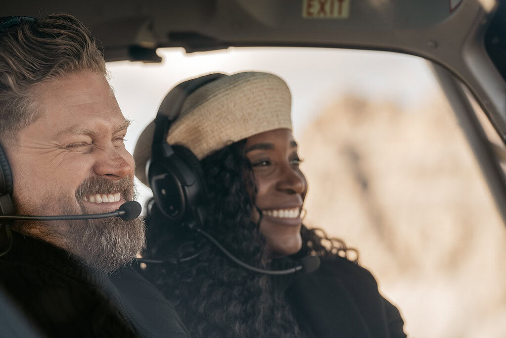 Smiling couple wearing headsets in helicopter cockpit.
