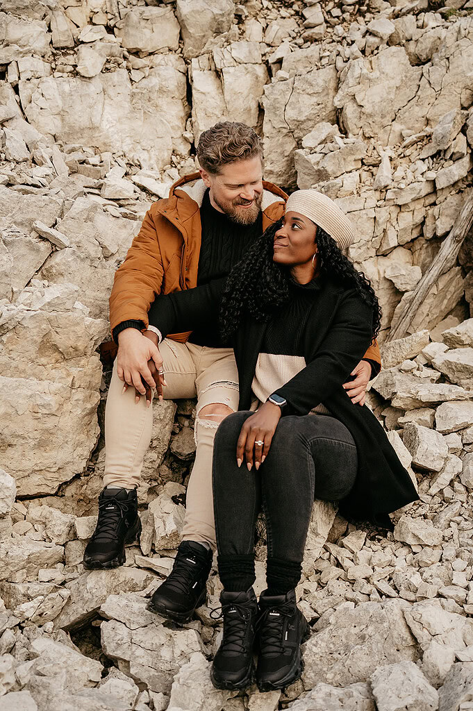 Couple sitting together on rocky terrain, smiling lovingly.