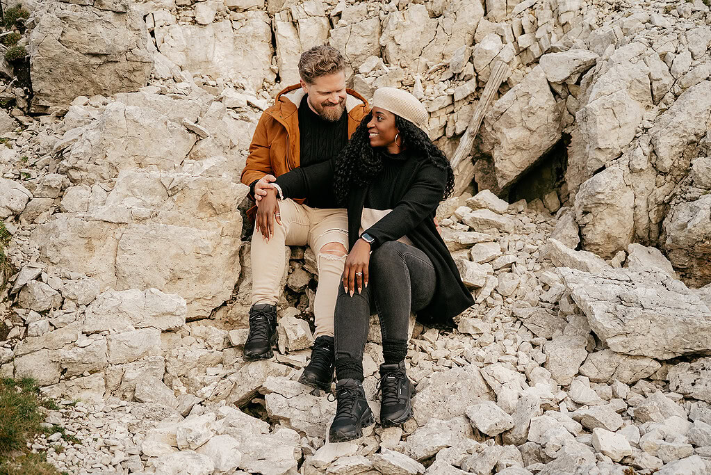 Couple sitting on rocky terrain, holding hands, smiling.