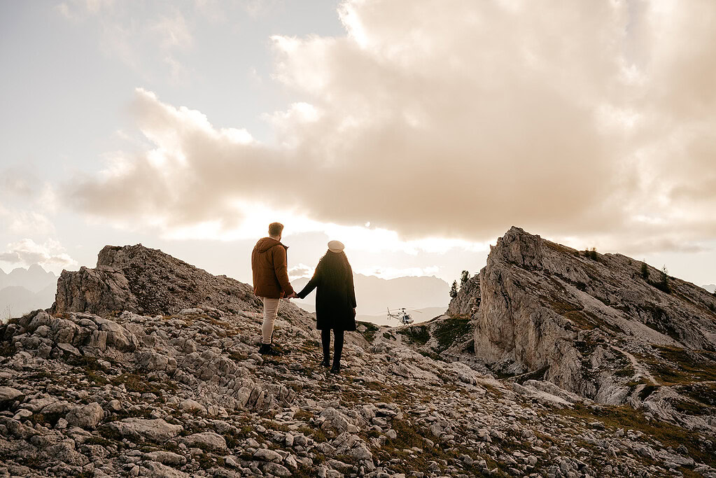 Couple holds hands on rocky mountain landscape.