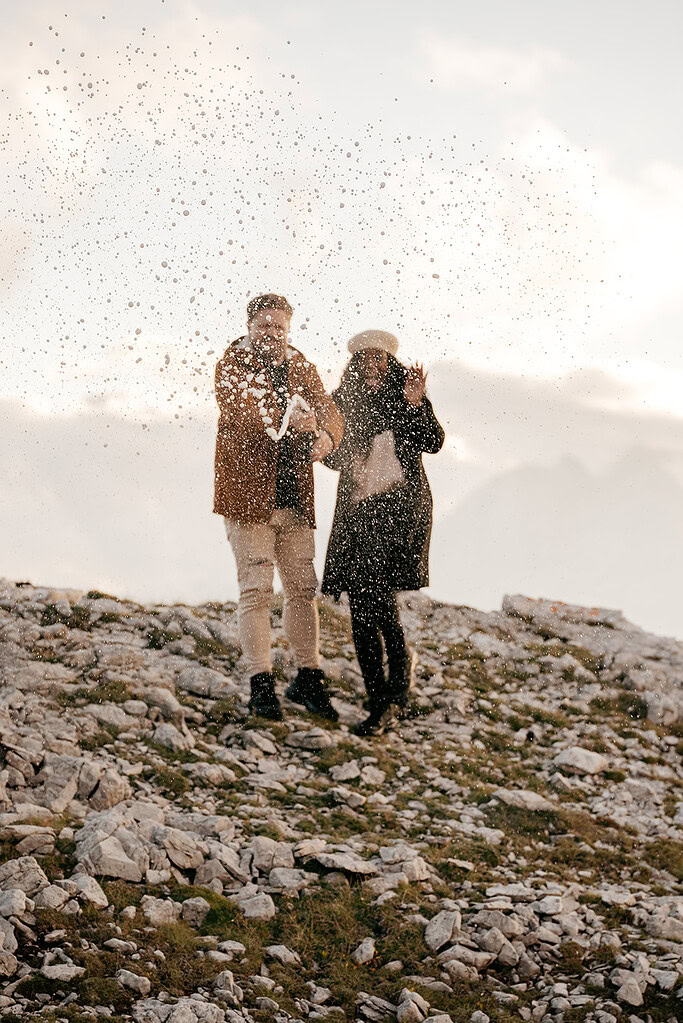 Couple celebrating outdoors, champagne spray in air.