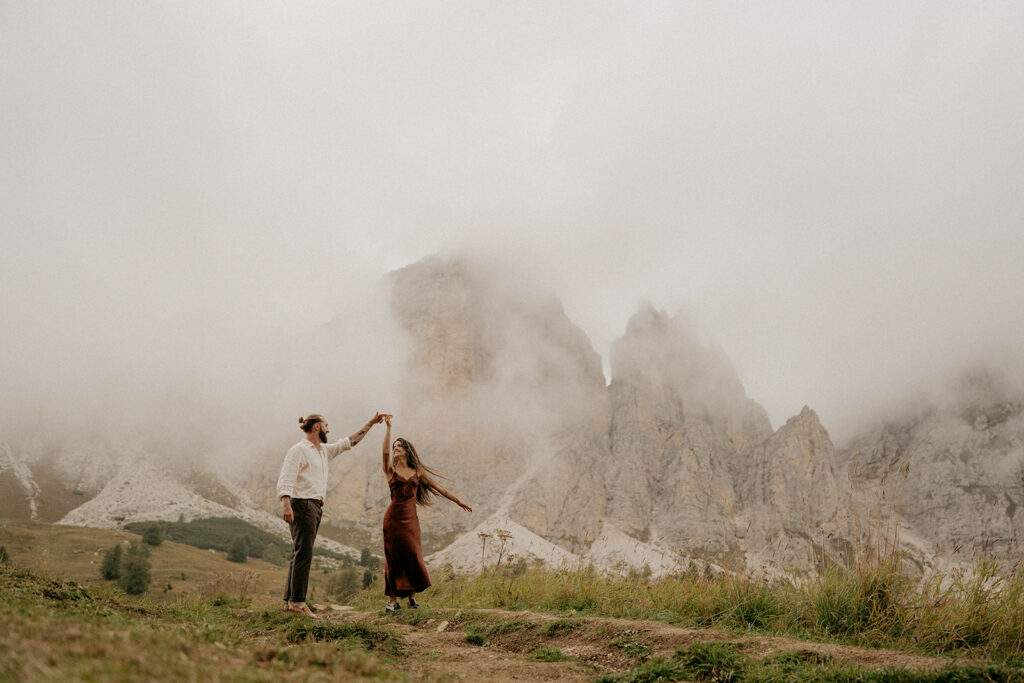 Couple dancing in front of misty mountain landscape.
