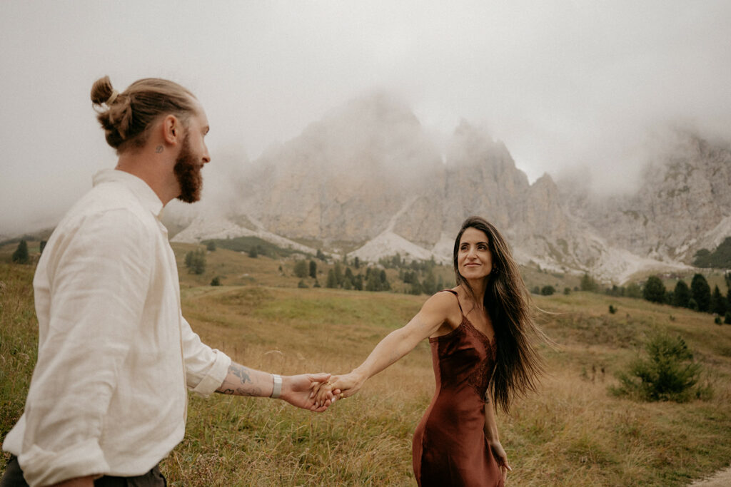 Couple holding hands in misty mountain landscape.