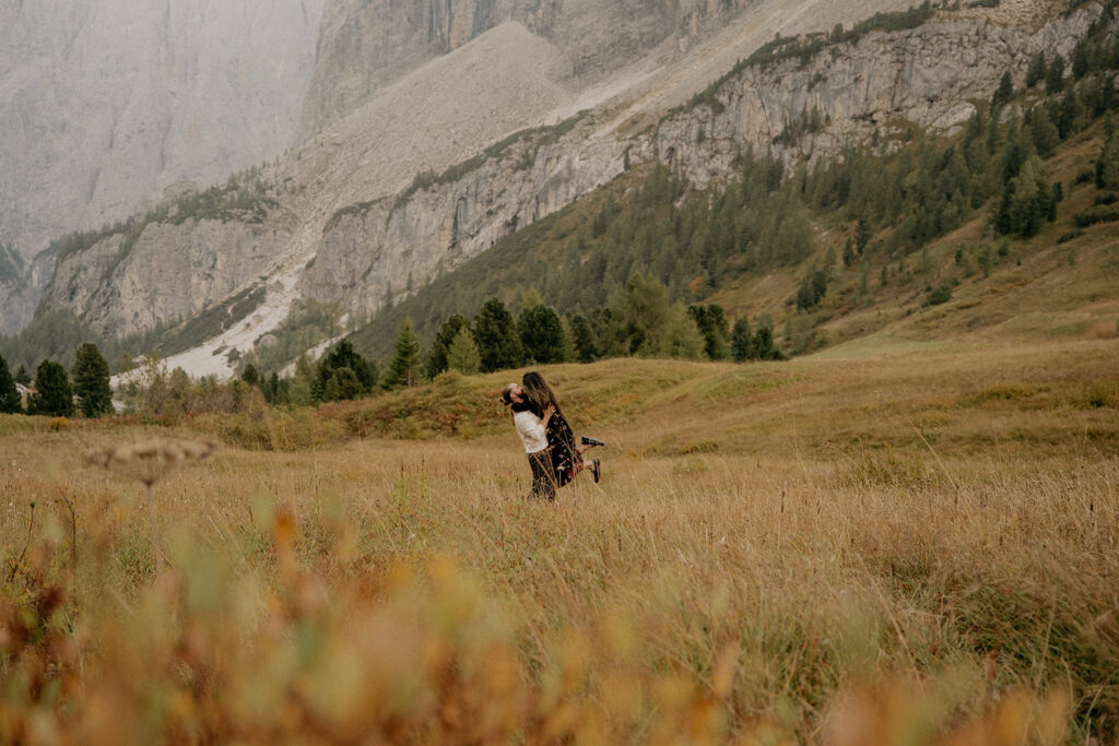Couple embraces in mountain meadow landscape.