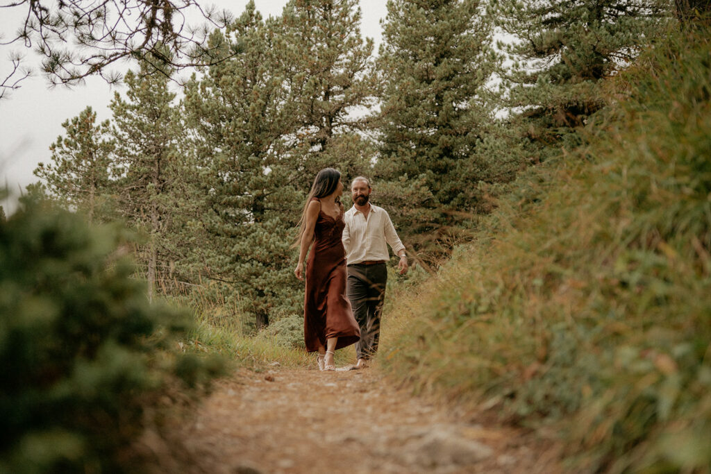 Couple walking on forest path surrounded by trees.