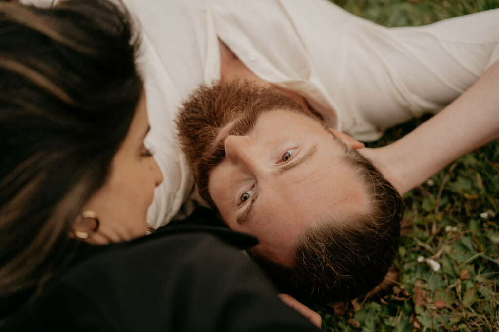 Couple lying on grass, sharing a tender moment.