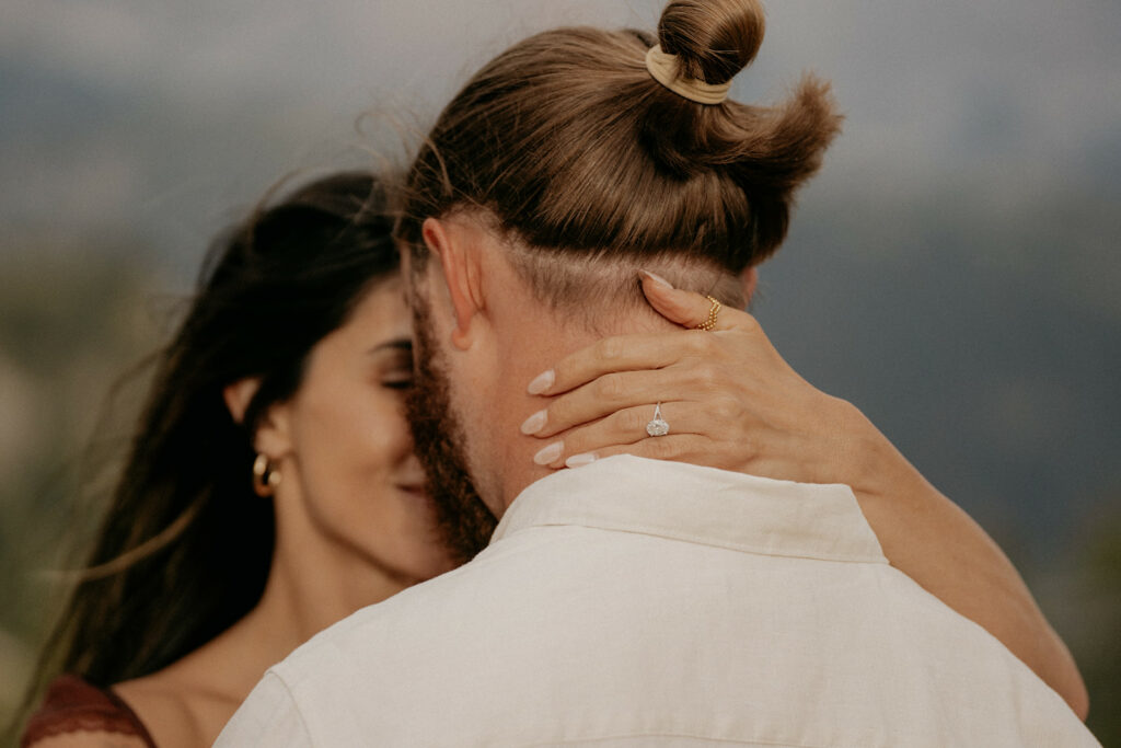 Close-up couple embracing with engagement ring visible.
