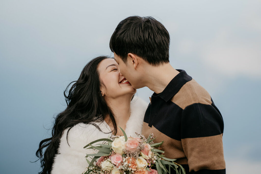 Couple kissing with flower bouquet outdoors.