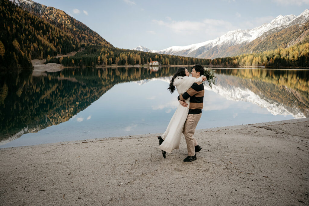 Couple embraces by mountain lake with snowy peaks.