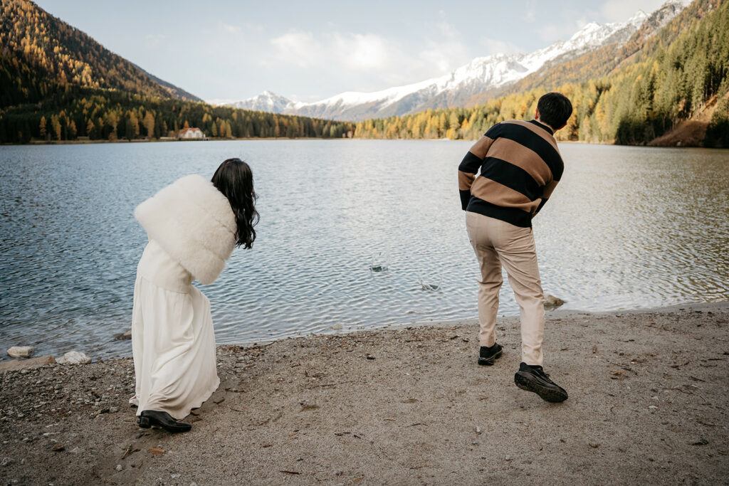 Couple skipping stones on mountain lake shore.
