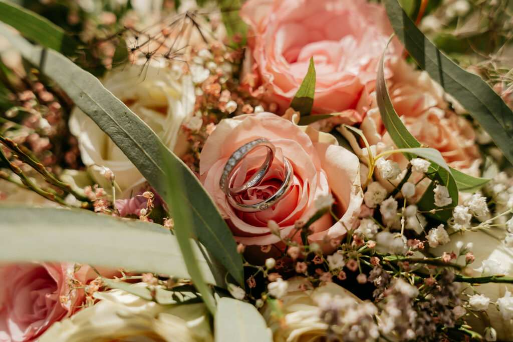 Wedding rings on pink roses and greenery bouquet.