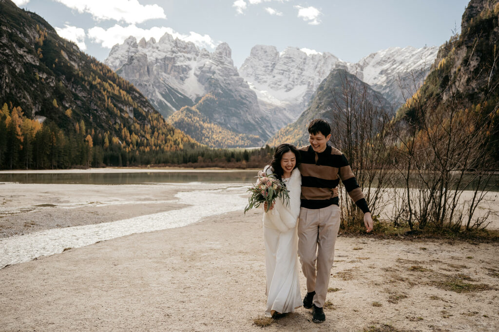 Couple walking by lake with snowy mountains backdrop.