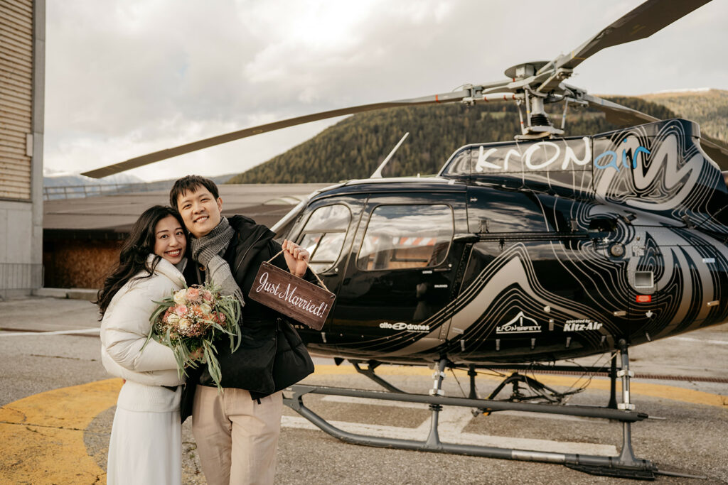 Newlyweds holding just married sign beside helicopter.