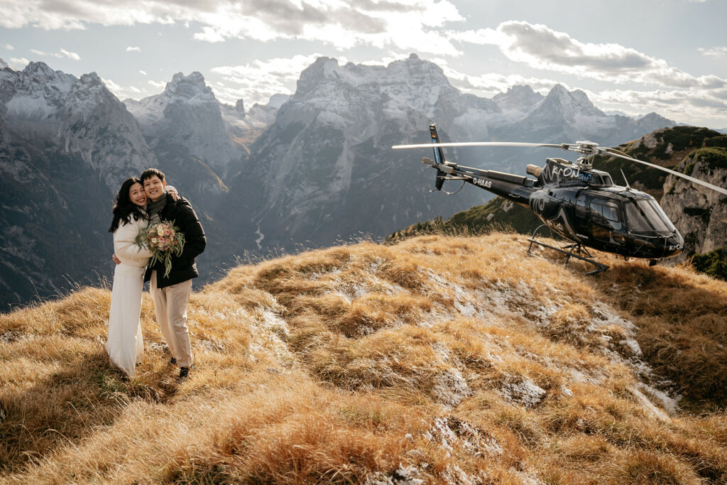 Couple embraces on mountain with helicopter nearby.