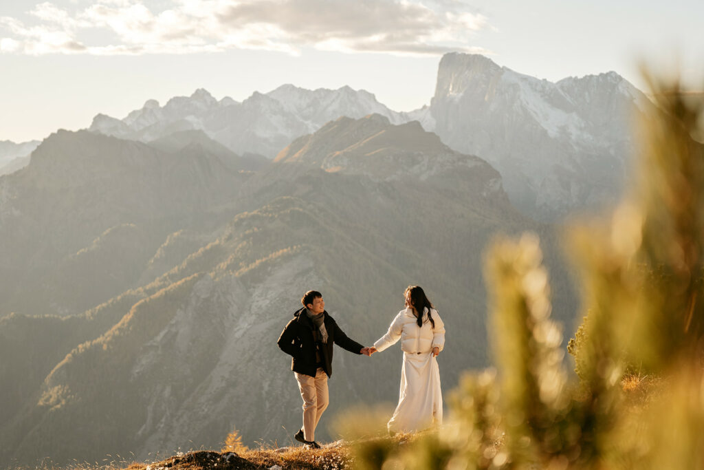Couple holding hands on mountain overlooking valley.