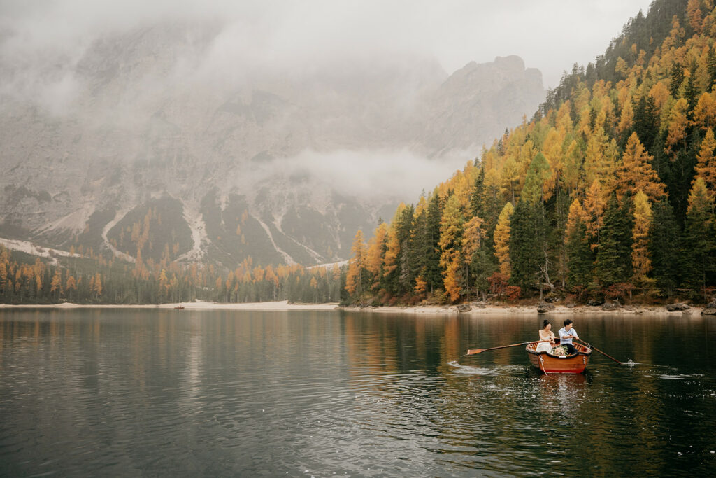 Couple rowing boat on lake with autumn trees.