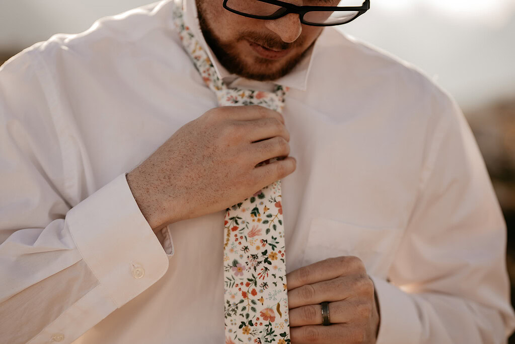 Man adjusts floral tie on white shirt.