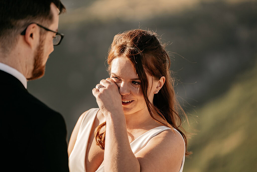 Emotional bride wipes tear during outdoor wedding ceremony.